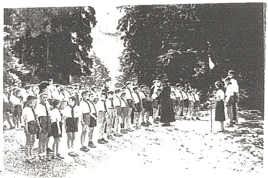 Page 17 de l'album, datée 1956 : enfants au garde-à-vous le long d'une allée, un prêtre en soutane présent.
