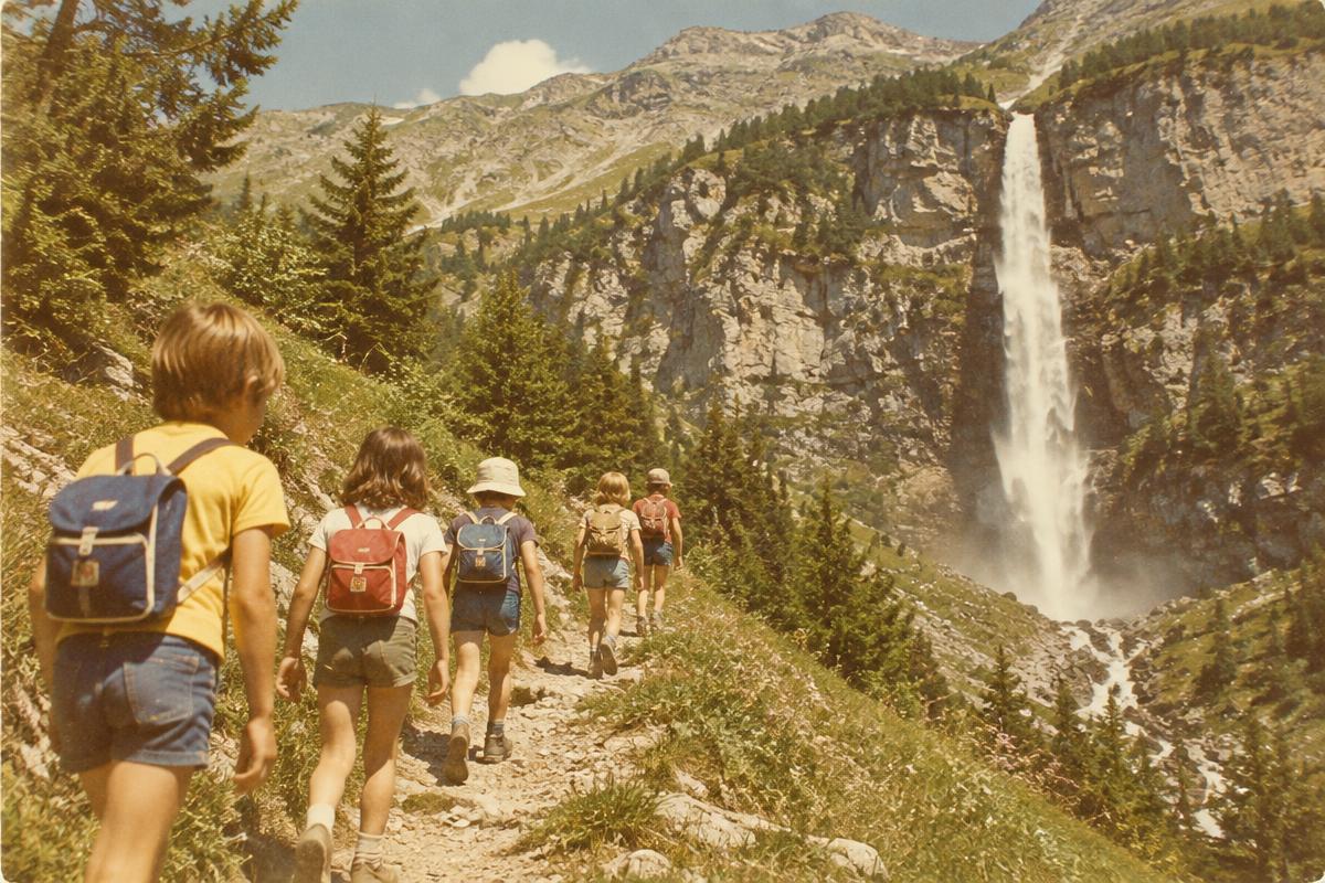 Photo vintage d'enfants de la colonie en randonnée sur un sentier alpin, face à une grande cascade du cirque